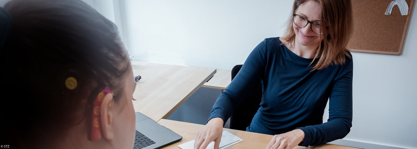 Eine Mitarbeiterin berät eine junge Frau mit Cochela-Implantat