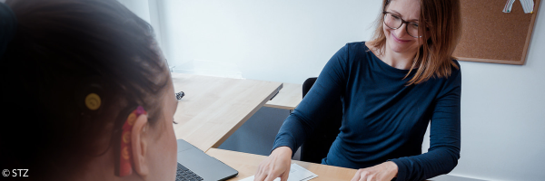 Eine Mitarbeiterin berät eine junge Frau mit Cochela-Implantat