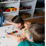 Gruppenraum im Kindergarten.Zwei Kinder und eine Erwachsene Person sitzen an einem Tisch und spielen ein Spiel. 